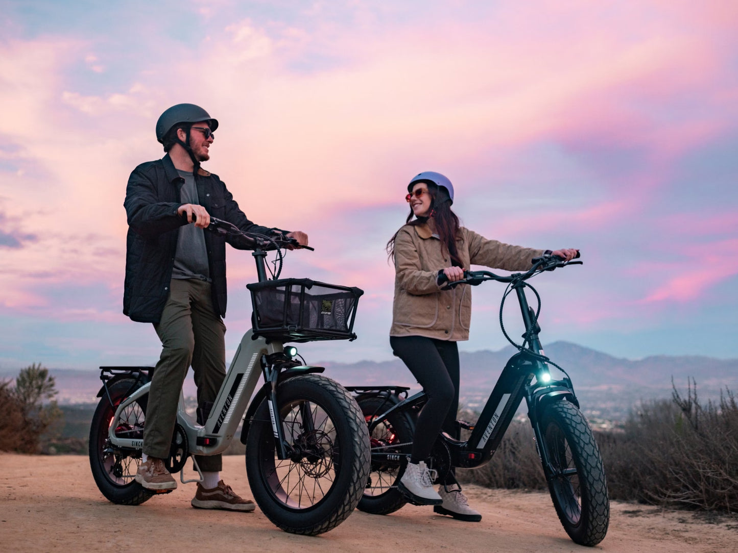 Aventon Sinch 2.5 Foldable Compact cargo eBike Couple on hard packed trail. Cotton candy colored sky in background