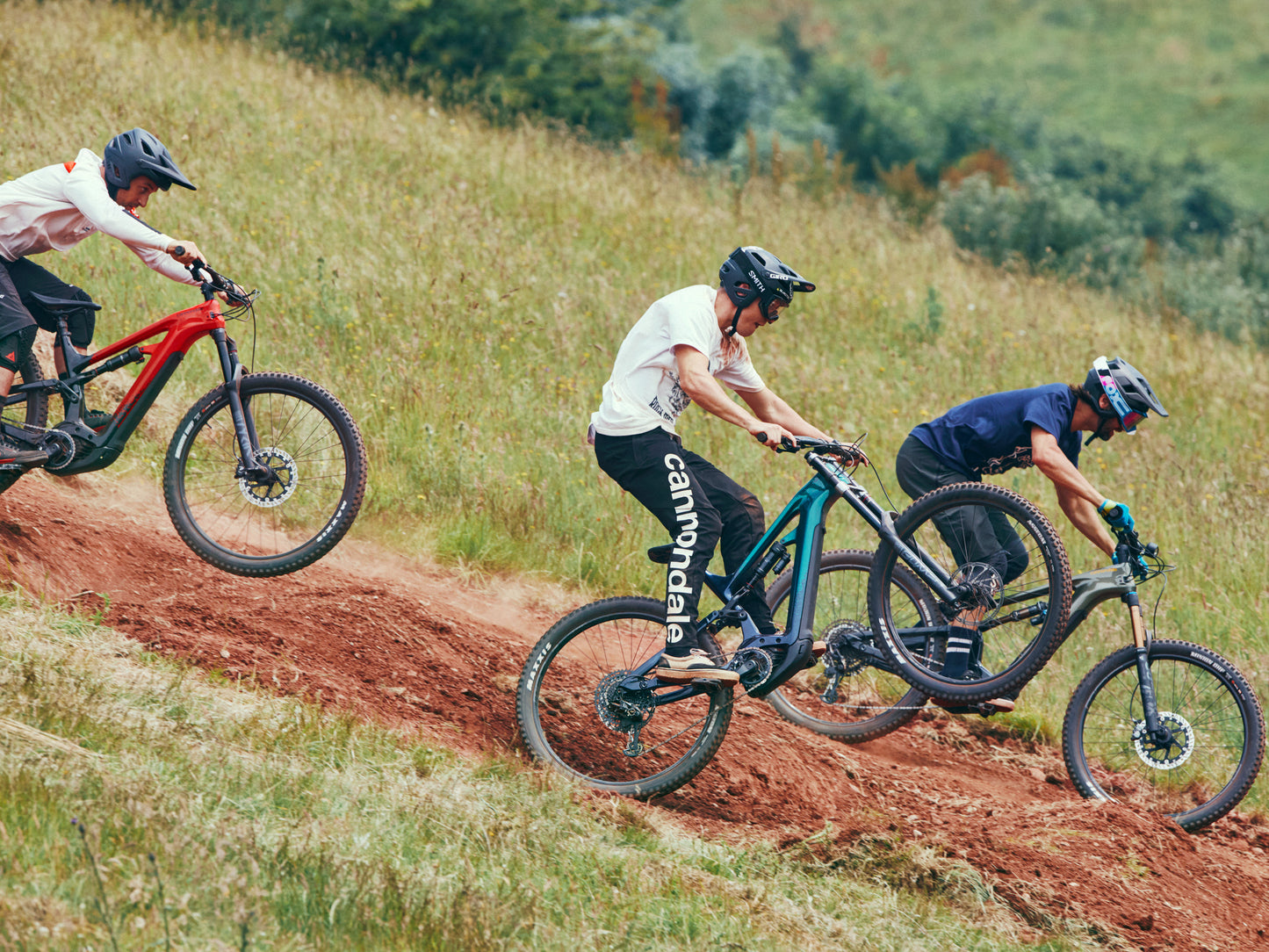 Cannondale Moterra Carbon Full Suspension eMTB Three riders going downhill on dirt track with green hills in background