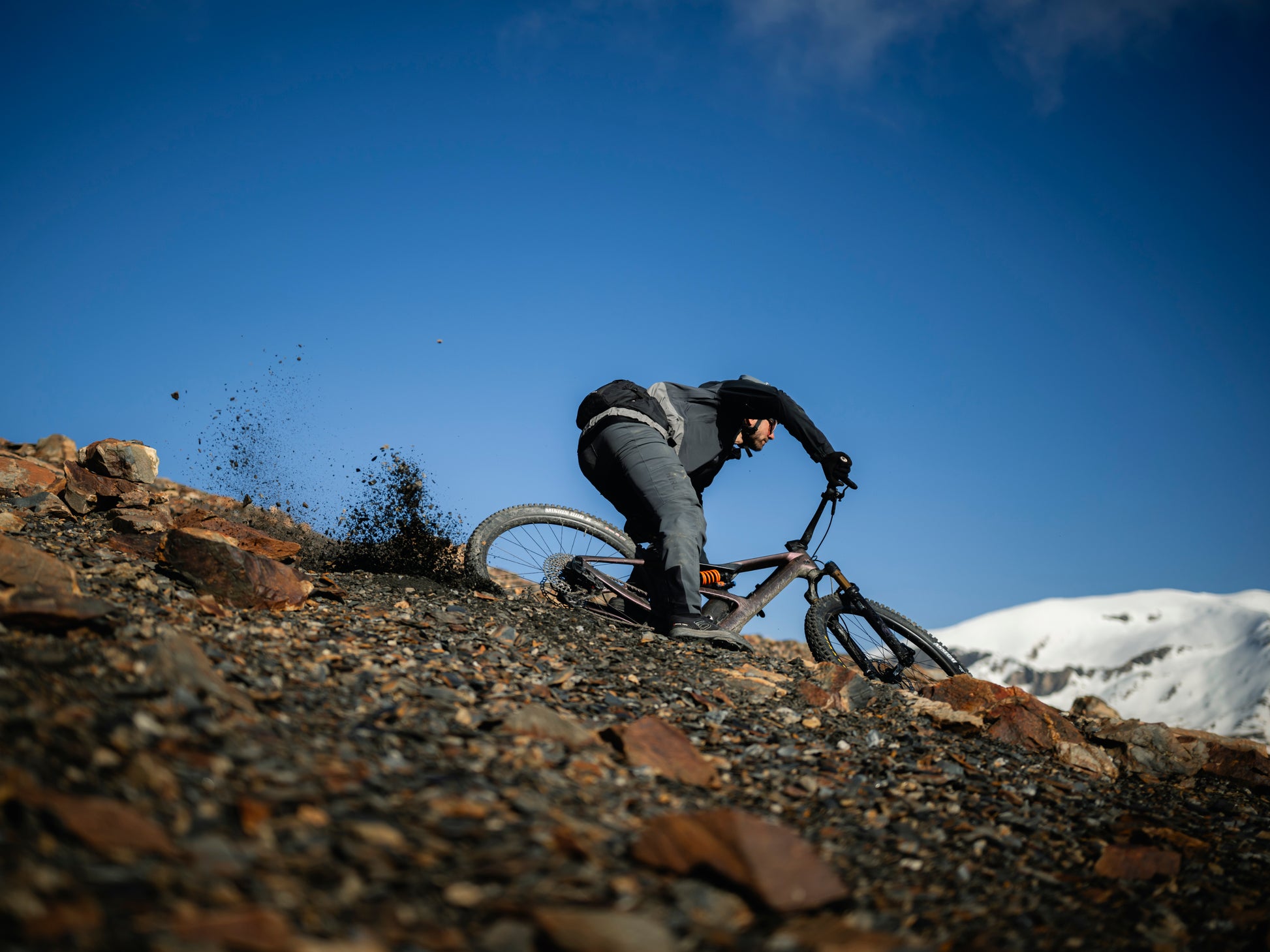 Orbea Occam LT Full Suspension Mountain bike Rider going downhill on rocky path with snowcapped hill in the background