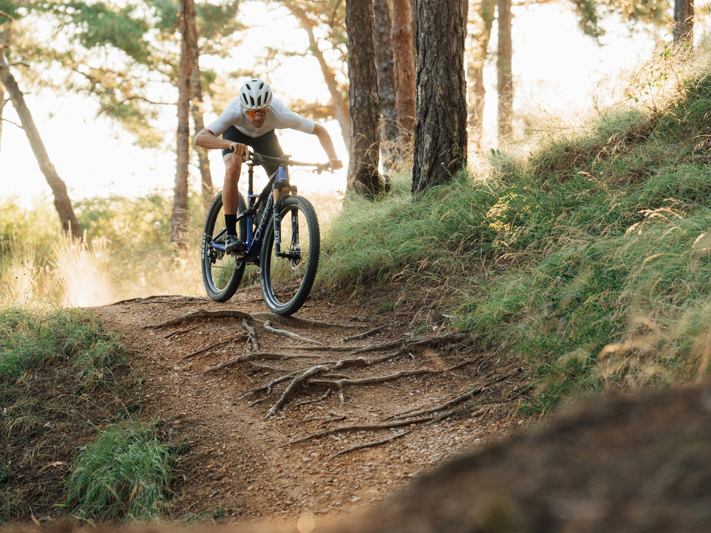 Orbea Oiz Full Suspension Mountain bike man riding down dirt single track with tree roots in path