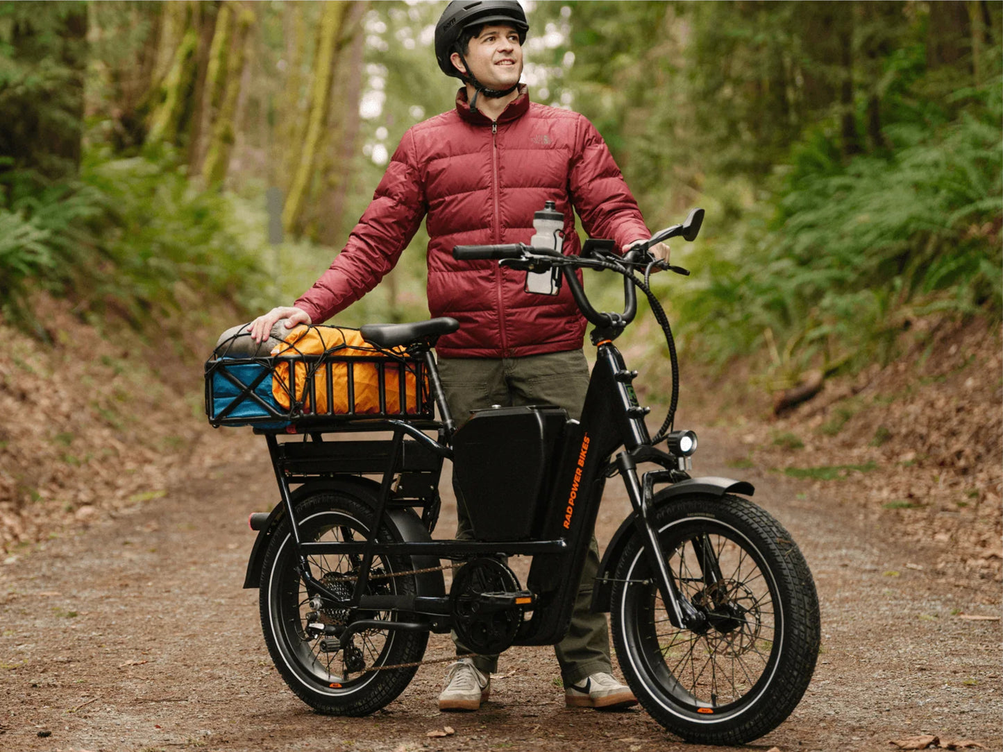 Rad Power RadRunner Max Electric Cargo Utility Bike. Man parked on a tree lined dirt path with cargo loaded on the bike