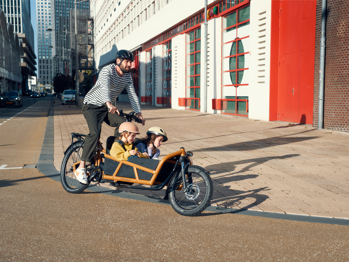 Riese & Muller Cargo Electric Bike. Male rider with two children in the cargo area. Family ride on city streets