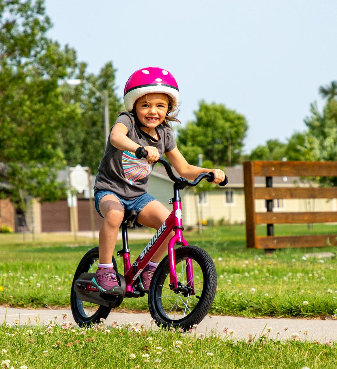 Strider 14x Convertible bike Classic Fuschia Child striding on a park path
