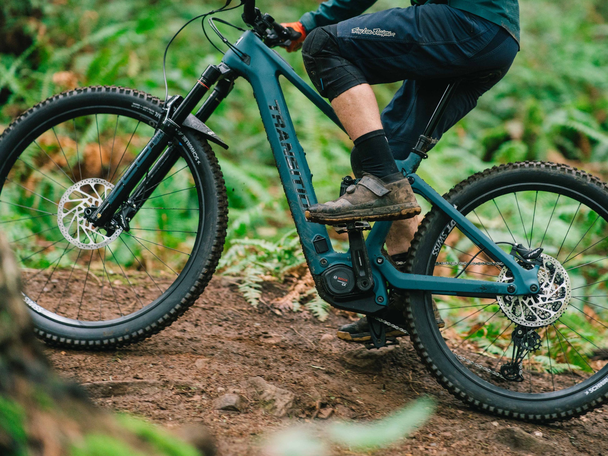 Transition Regulator CX Carbon Full suspension eMTB Salish sea blue Closeup of Bosch CX motor Muddy rider on forest trail