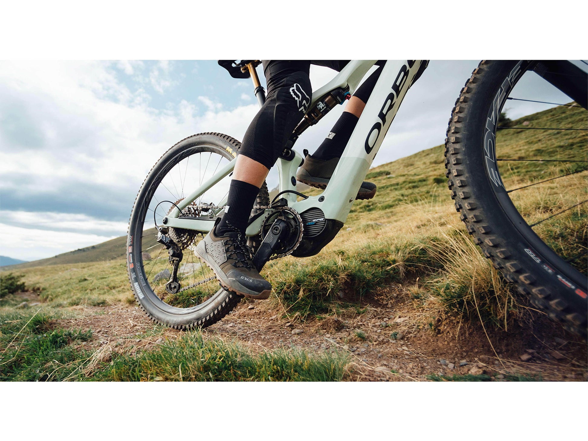 closeup action shot of an Orbea Rise M10 e-mountain bike in sap white green fog gloss