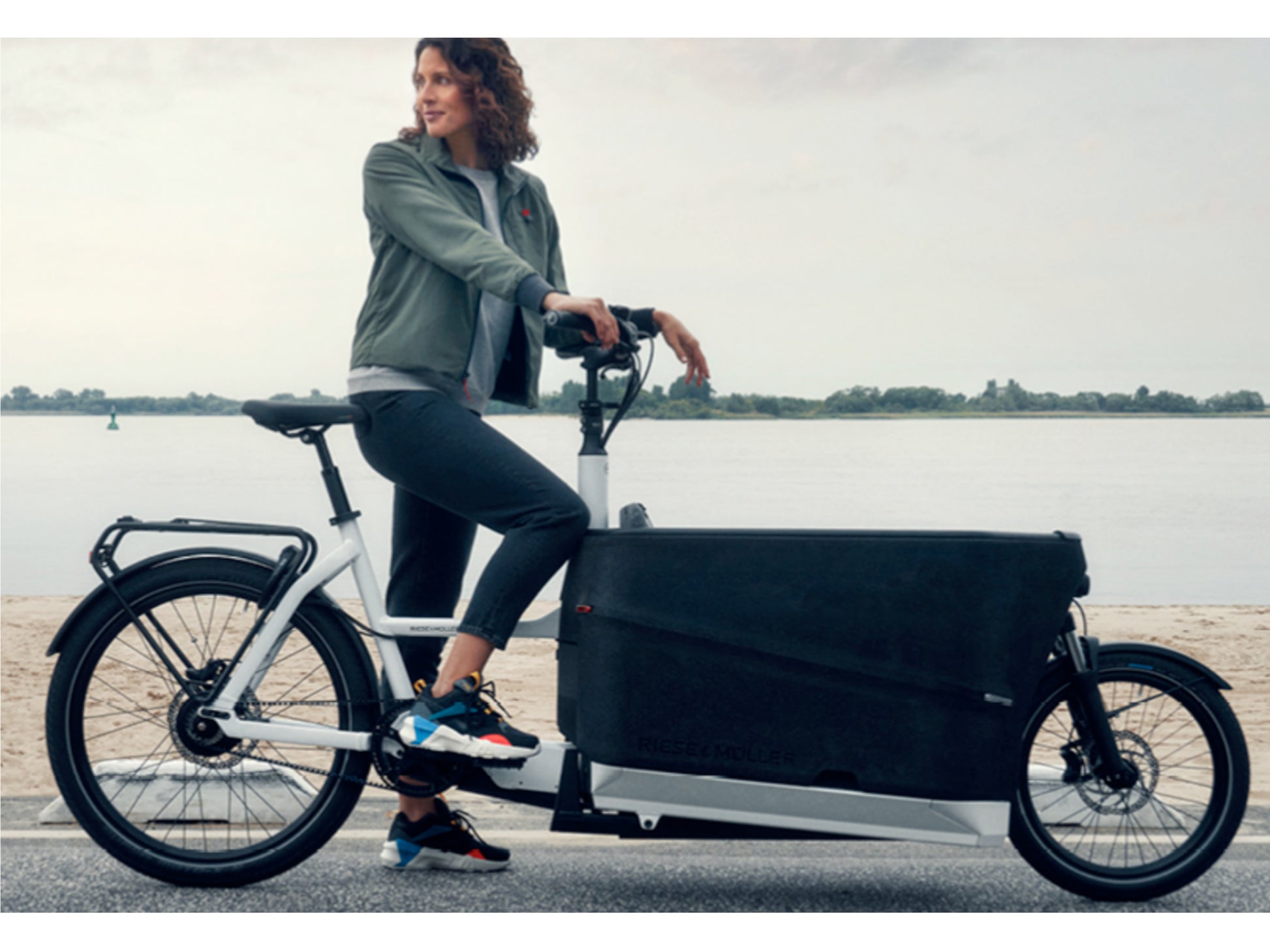 Riese & Muller Packster 70 Family cargo eMTB hardtail woman standing with bike by waterfront
