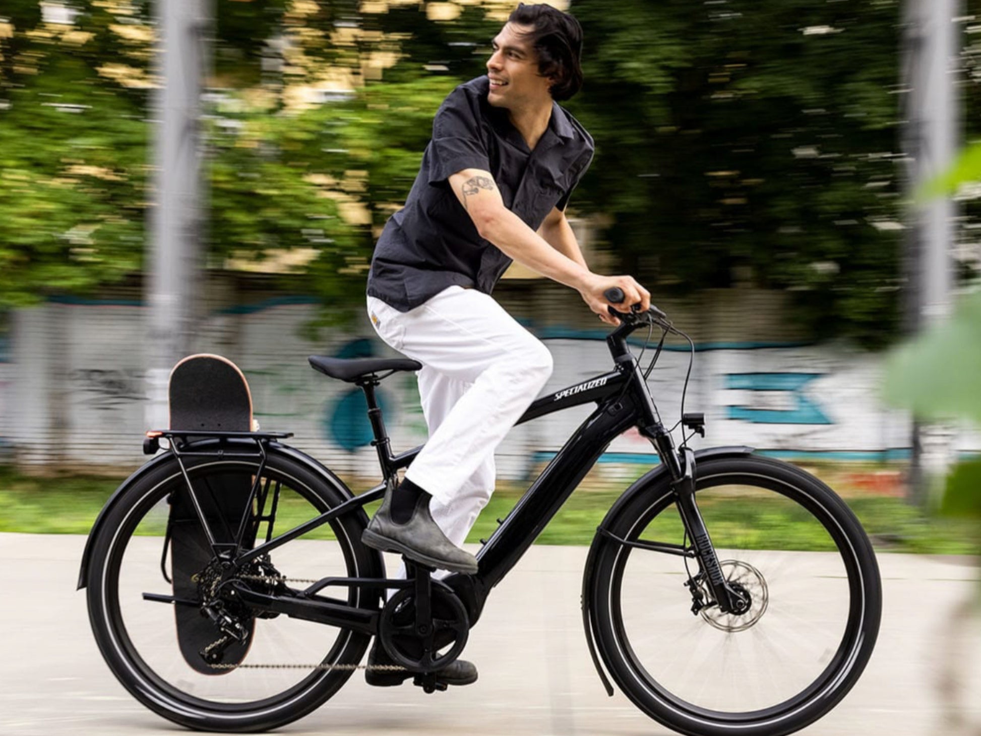 Specialized Turbo Vado 5.0 IGH eMTB hardtail man riding city street with skateboard in rear carrier