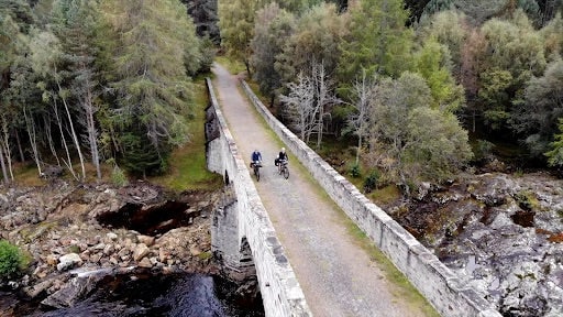 Two people riding electric bikes on a bridge in Scotland