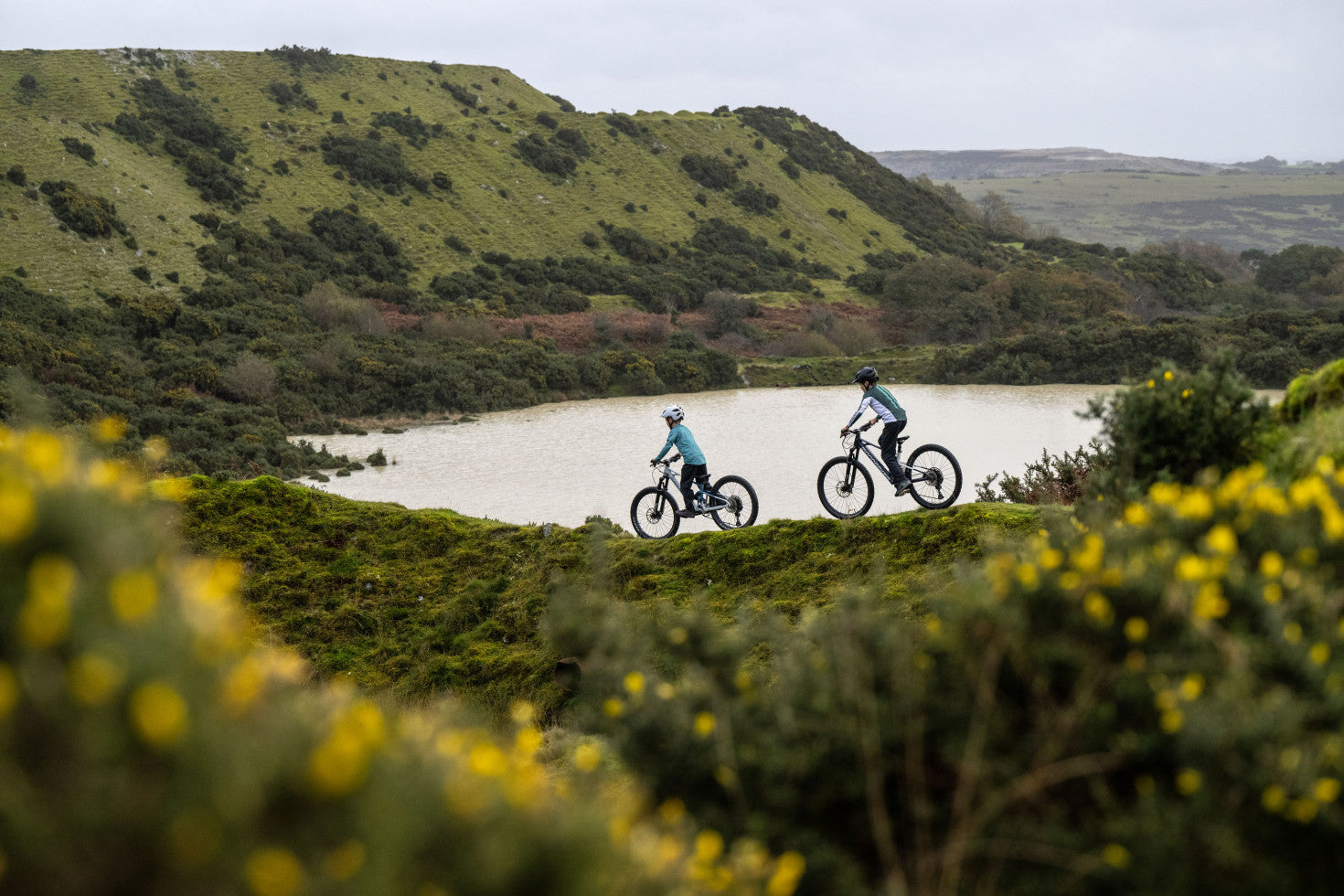 Mondraker F-Play 26 Children's eMTB Riding along the lakeside with surrounding green hills 
