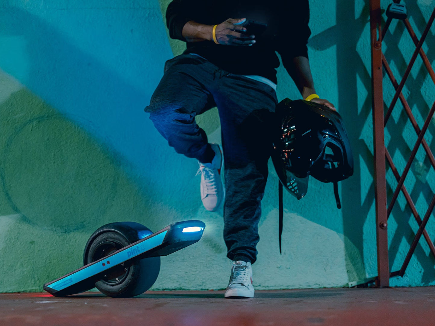 OneWheel Pint X Board in Powder blue. Guy leaning on wall, holding his helmet and checking phone.