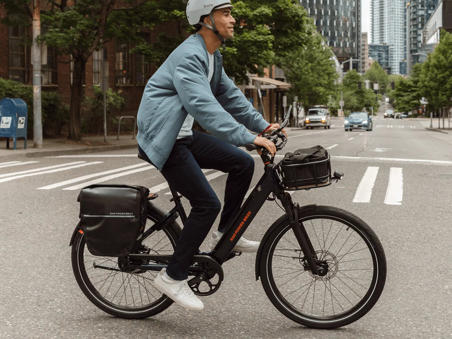 Rad Power RadKick™ Belt Drive Electric Lightweight Bike Midnight blue Man riding across a city crosswalk. Shown with optional accessories