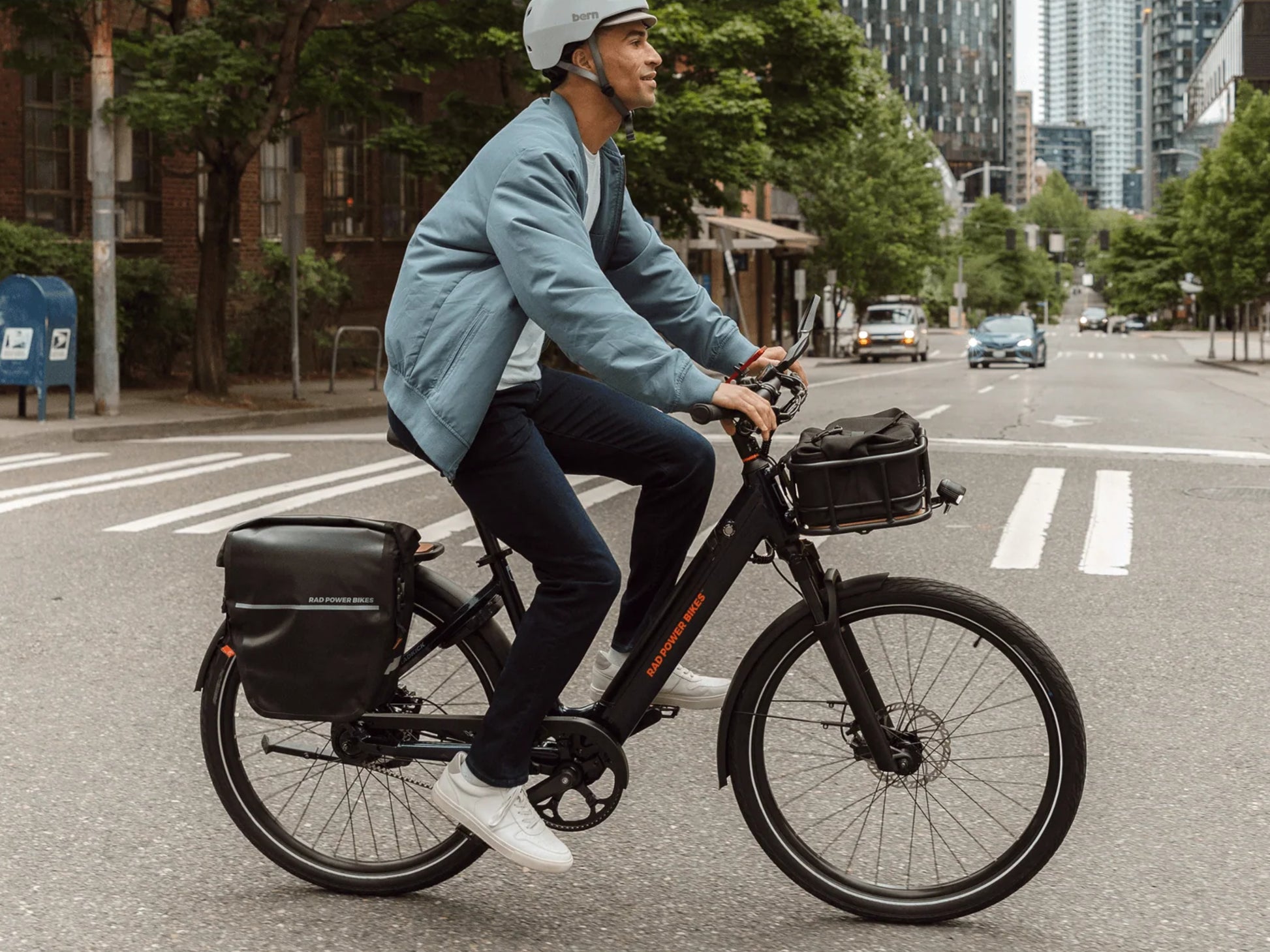 Rad Power RadKick™ Belt Drive Electric Lightweight Bike Midnight blue Man riding across a city crosswalk. Shown with optional accessories