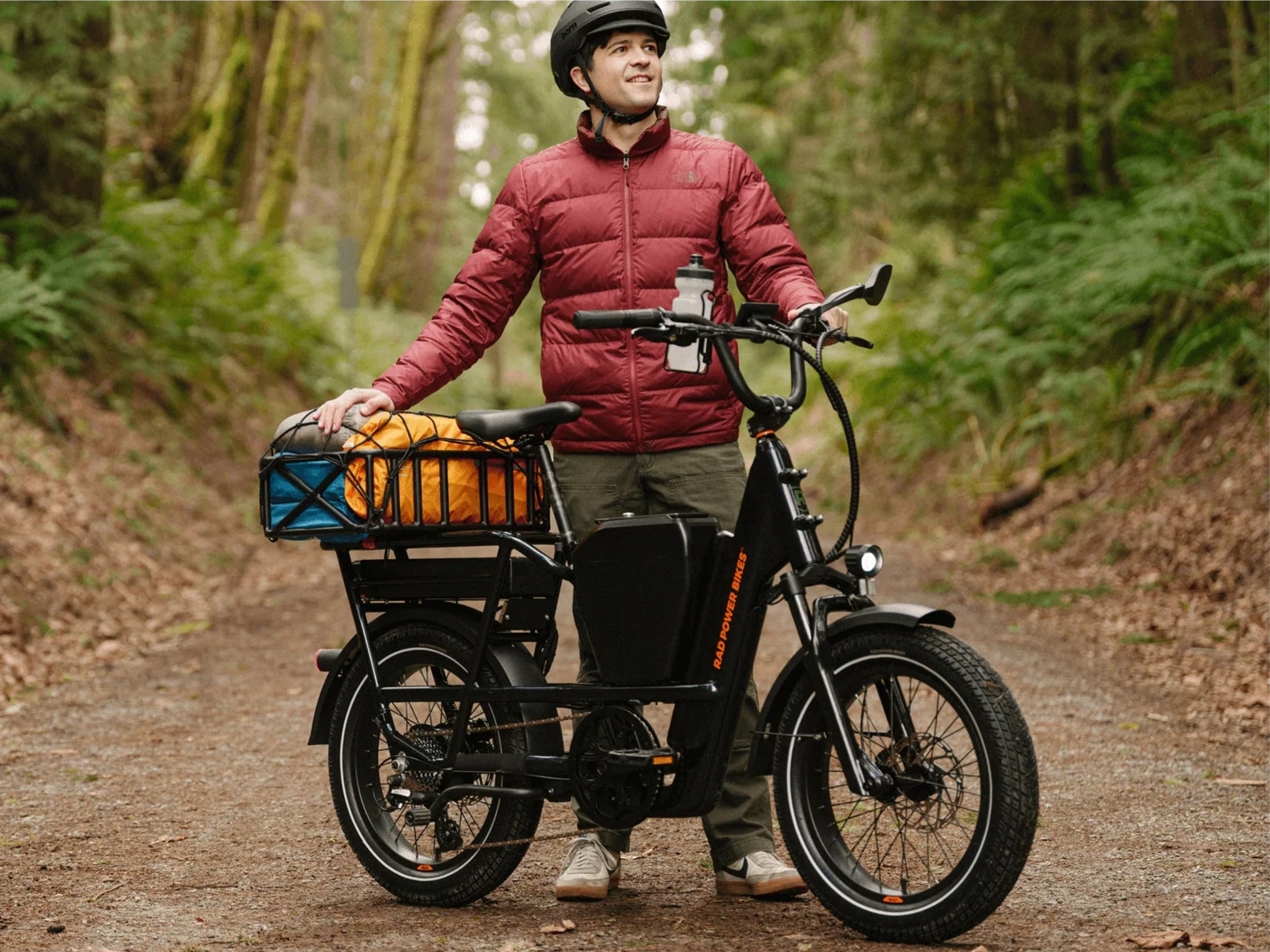 Rad Power RadRunner Max Electric Cargo Utility Bike. Man parked on a tree lined dirt path with cargo loaded on the bike