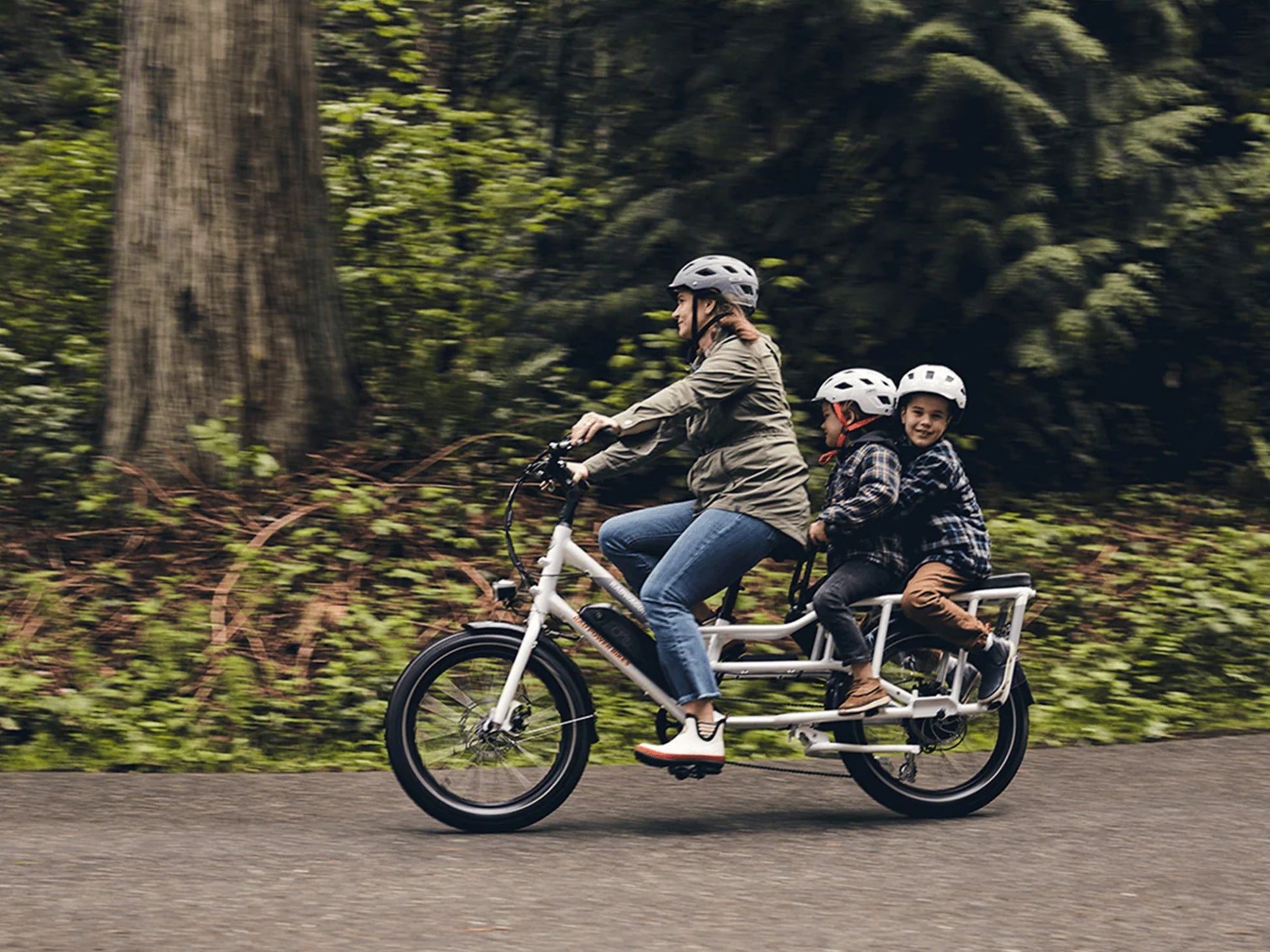 Rad Power RadWagon 4 Electric Cargo bike. Mom and two kiddos riding on a paved path. Trees in the background