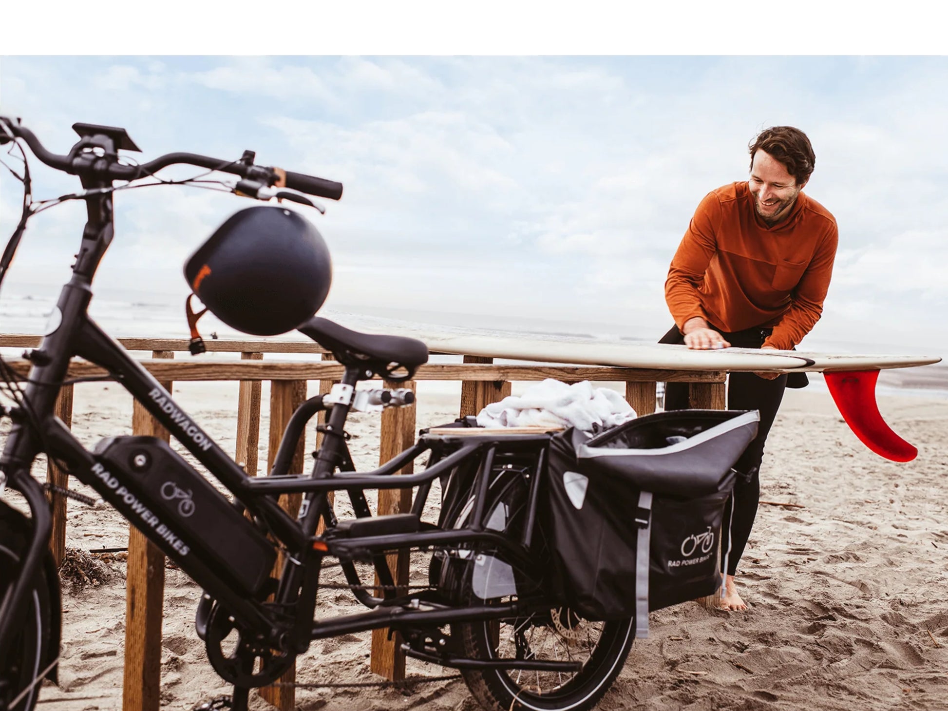 Rad Power RadWagon 4 Electric Cargo bike. Surfer waxing surboard. RadWagon parked on beach wtih cargo bags shown