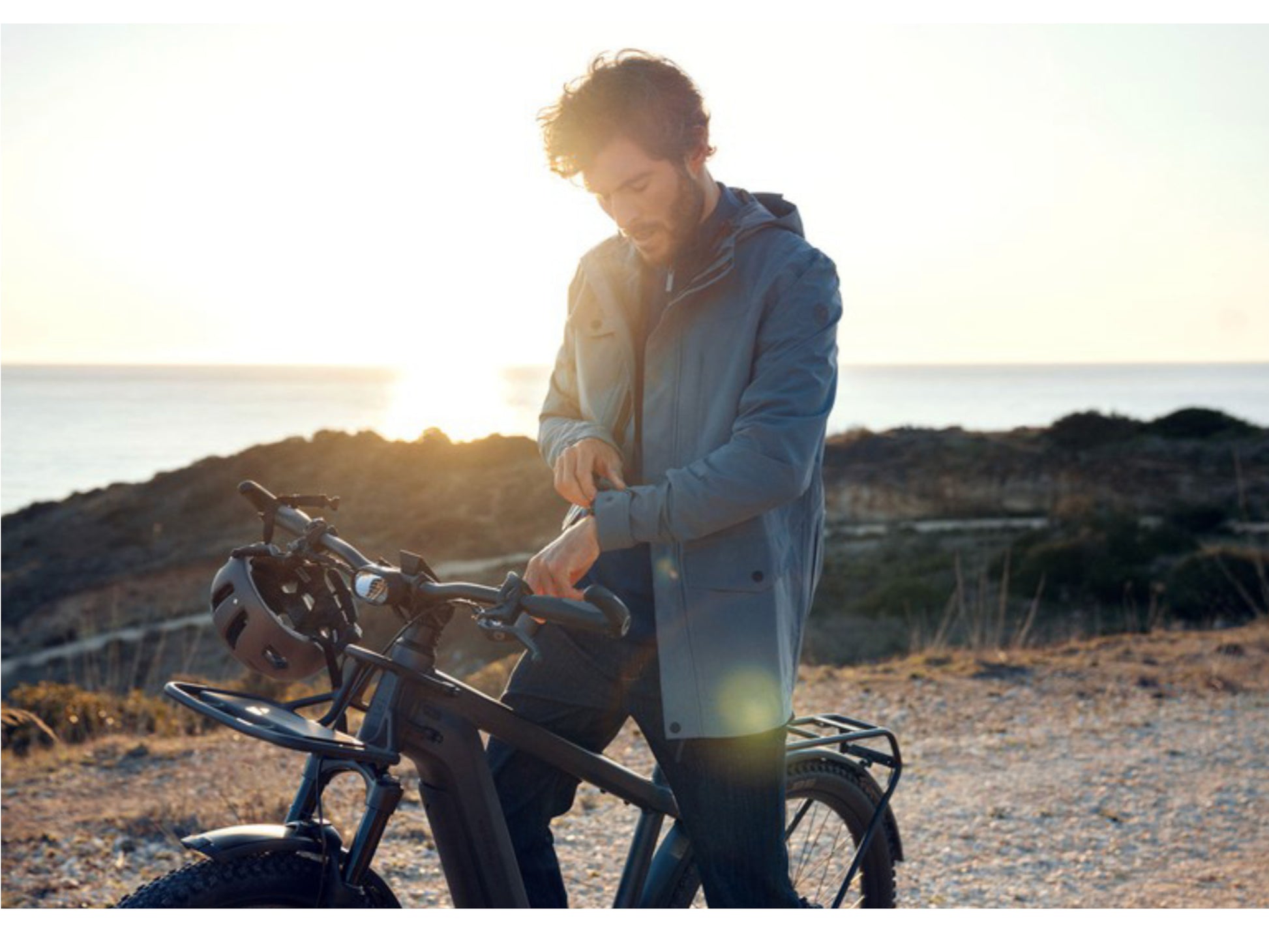 Riese & Muller Charger. Man stops on gravel roadside to check his watch. Ocean in the background