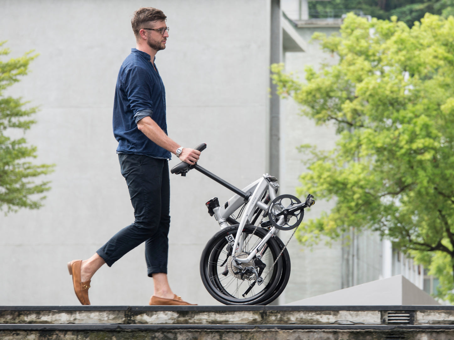 Tern Porter + Saddle Lifestyle. Man wheeling bike by the saddle down a city street