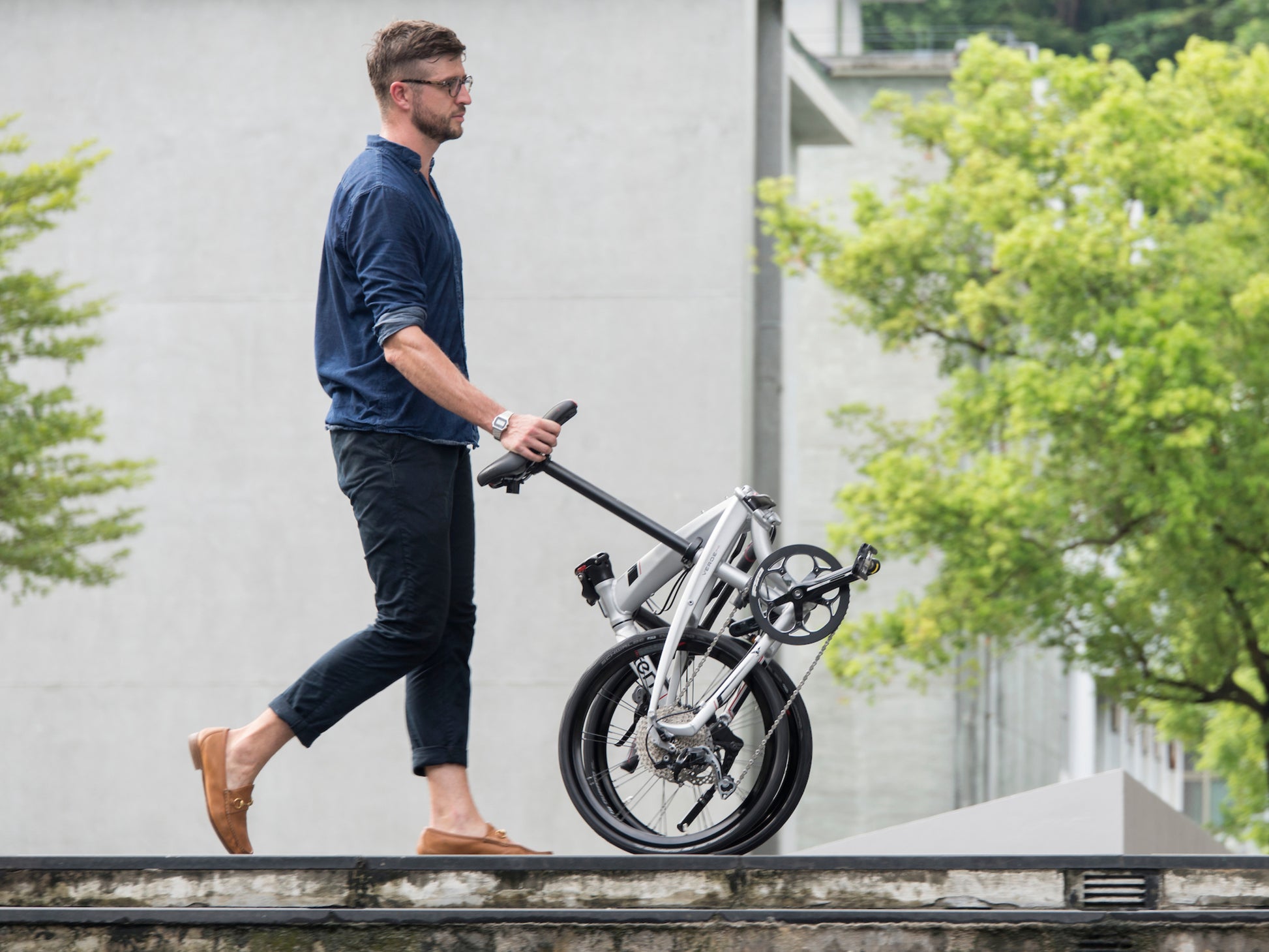 Tern Porter + Saddle Lifestyle. Man wheeling bike by the saddle down a city street