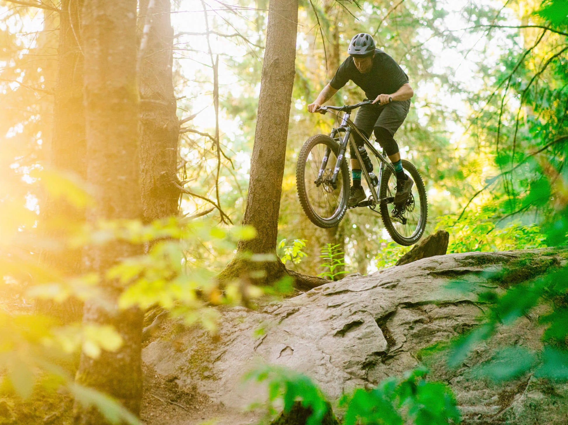 Transition TransAm NX Steel Hardtail mountainbike Chrome Lifestyle. Rider rock hopping on forest trail in mountain setting