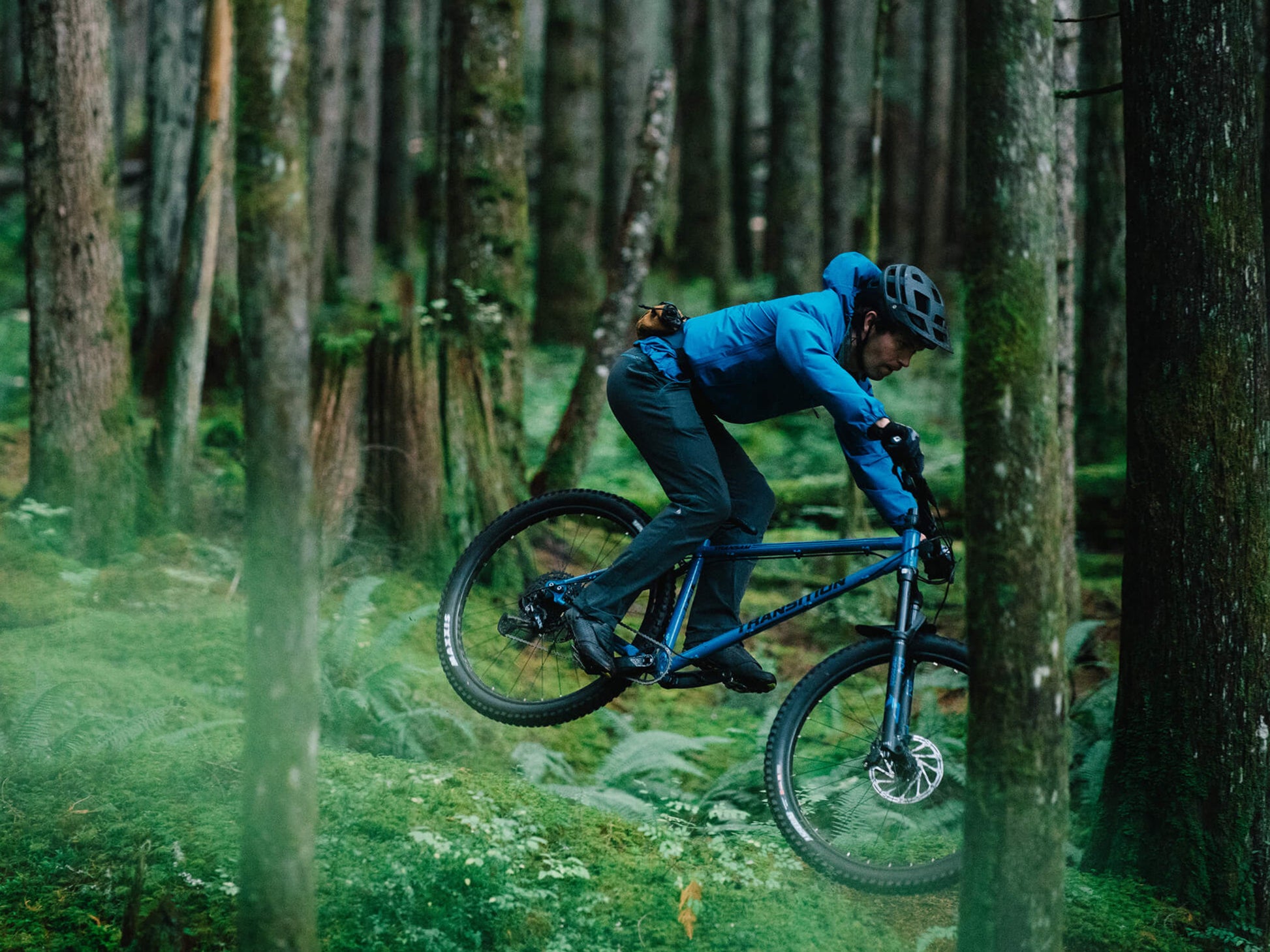 Transition TransAm NX Steel Hardtail mountainbike Cobalt blue Lifestyle. downhill rider on forest trail in mountain setting