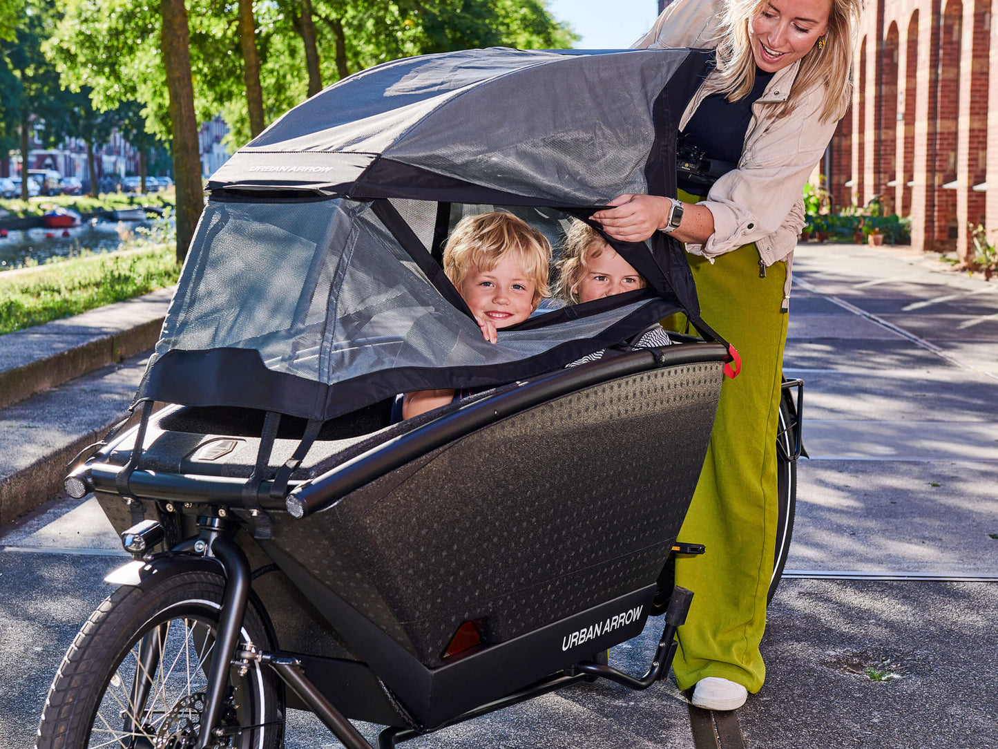 Urban Arrow Family Suncover shown with two children on board and a woman standing on the side